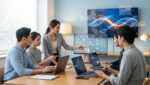 Four people gathered around a table with laptops and tablets in a bright modern office setting